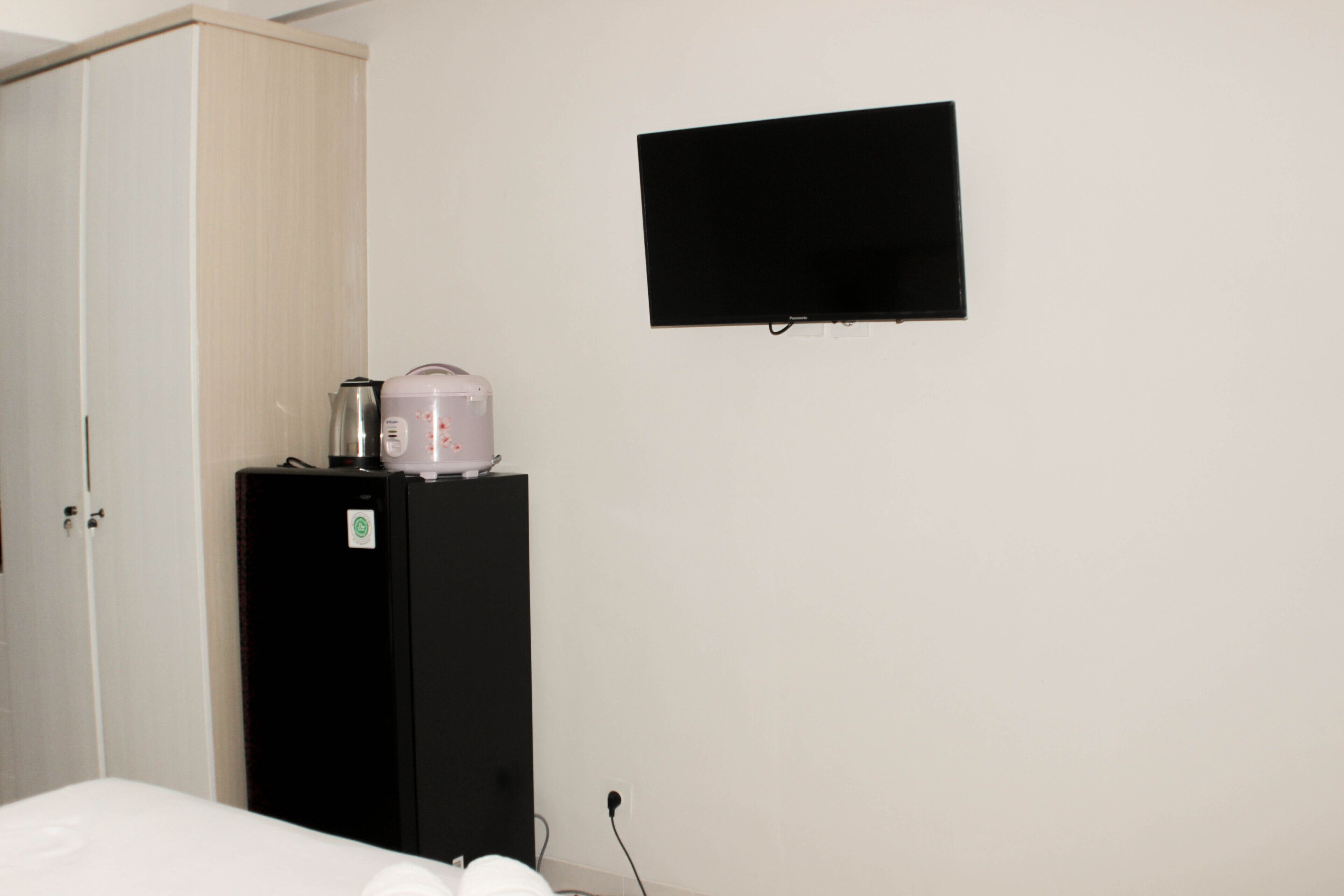 Une chambre comprenant un lit, une armoire, un réfrigérateur noir et un téléviseur à écran plat fixé au mur.