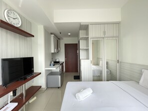 A hotel room with a bed, a TV, a kitchenette, and a bathroom. - Cozy Studio Apartment At Taman Melati Jatinangor (Hegarmanah)