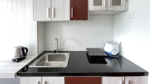 Una cocina con encimera negra, pileta de acero inoxidable y muebles blancos.