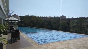 Una piscina con borde de baldosas, rodeada de plantas en macetas y mobiliario de exterior.
