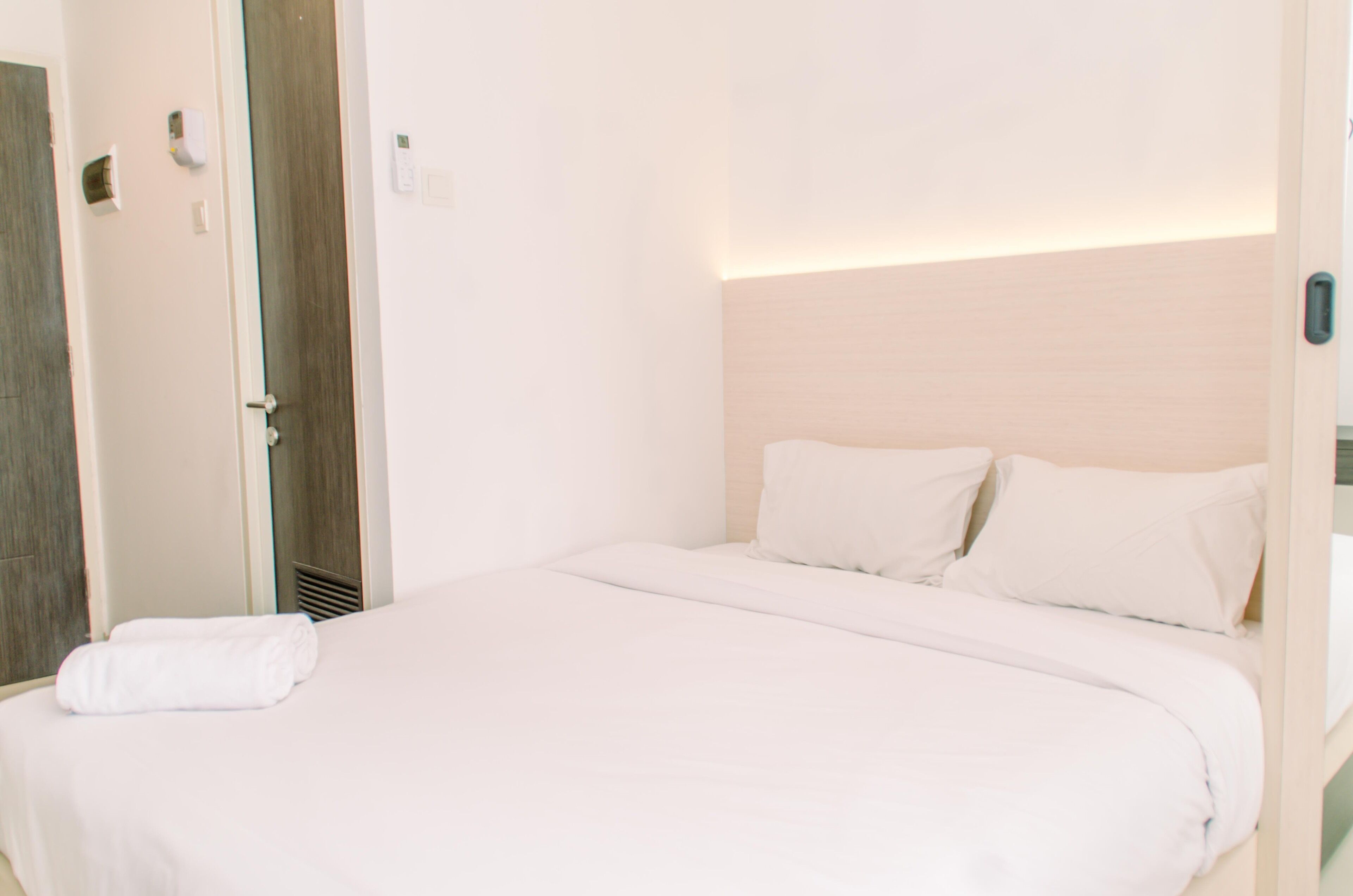 A hotel room with a neatly made bed, a wooden door, and a light-colored headboard.