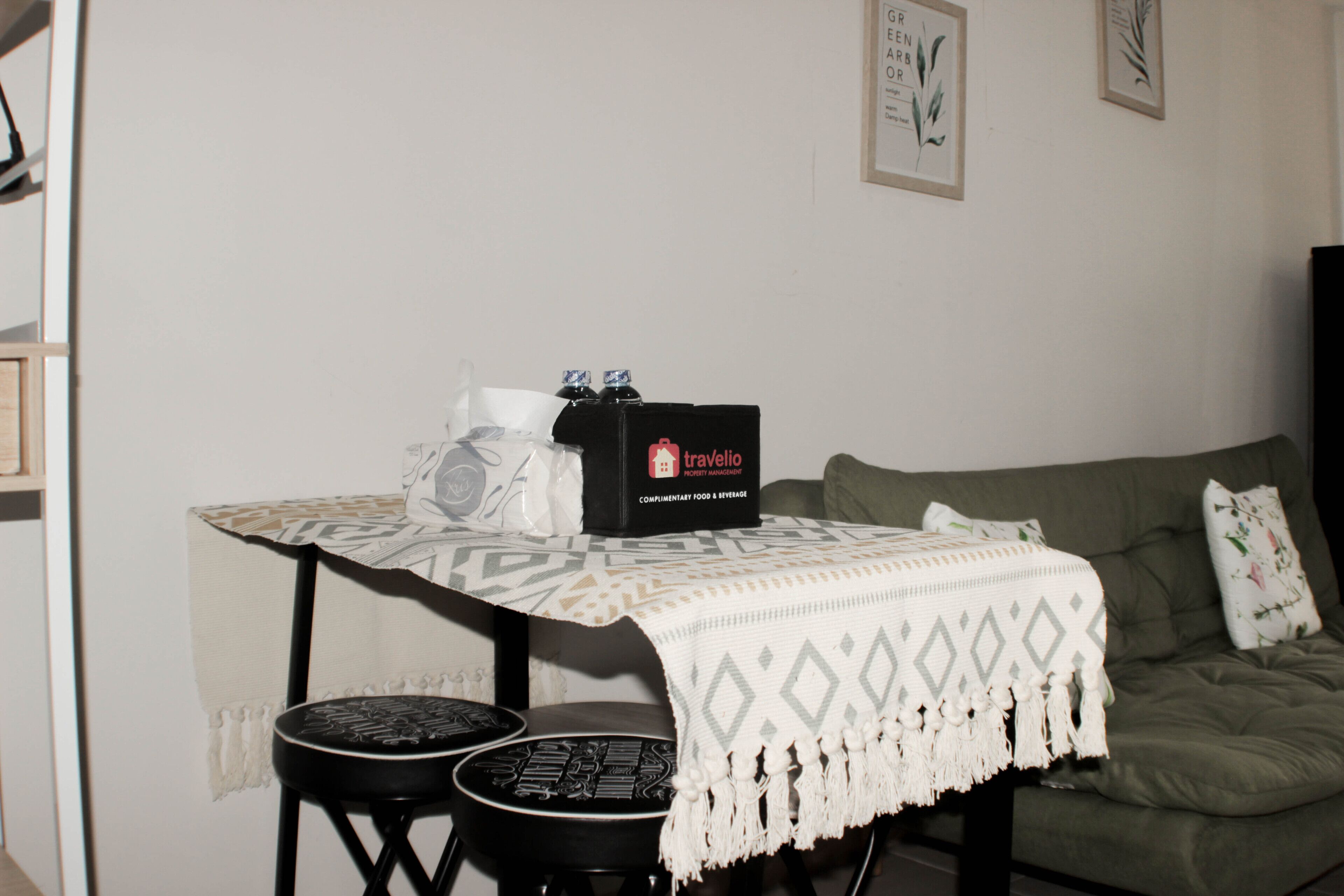 Una mesa pequeña con una bandeja, una caja etiquetada 'travelio' y un sofá verde en una habitación con paredes lisas.
