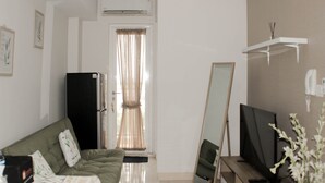 Een woonkamer met een groene bank, een zwarte koelkast, een televisie en een spiegel die tegen de muur staat.