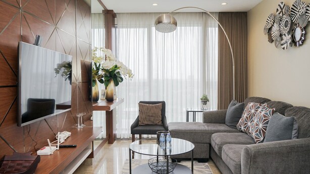 Een moderne woonkamer met een hoekbank, een glazen salontafel, een flatscreen televisie bevestigd aan een houten wand en een decoratief wandobject.
