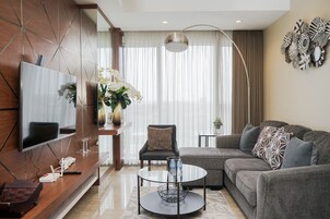 A modern living room with a sectional sofa, a glass coffee table, a flat-screen TV mounted on a wooden wall, and a decorative wall piece.