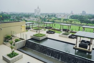 A rooftop garden with a water feature, seating areas, and a view of a distant white building.