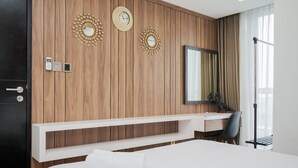 Een moderne hotelkamer met een wandpaneel van hout, een groot bed, een bureau met stoel, een spiegel en twee wandklokken.