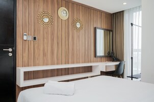 A modern hotel room with a wooden panel wall, a large bed, a desk with a chair, a mirror, and two wall clocks.