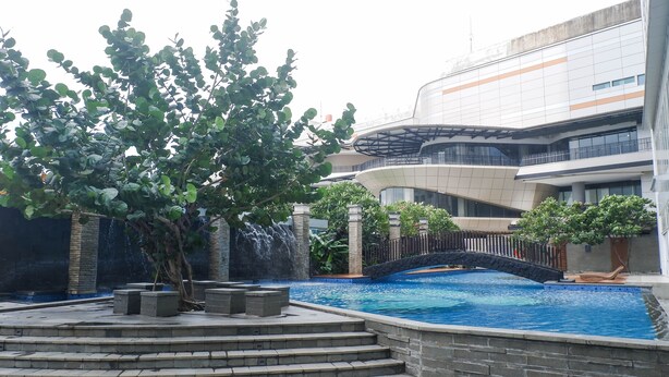 A modern building with a swimming pool, steps, and a bridge. - 3Br Luxurious And Elegant Apartment At Grand Sungkono Lagoon (Surabaya)
