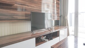 A modern living room with a flat-screen TV mounted on a wooden wall, a white cabinet below, and a large window with curtains.