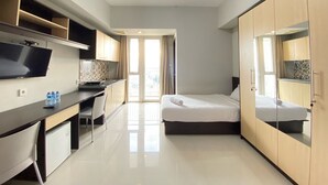 Una habitación de hotel compacta con kitchenette, una cama, un escritorio y un televisor.