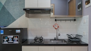 A kitchen with a black refrigerator, white tiled backsplash, a stainless steel range hood, a sink, and a black dish rack. - Fancy And Comfy Studio At B Residence Apartment (Pagedangan)