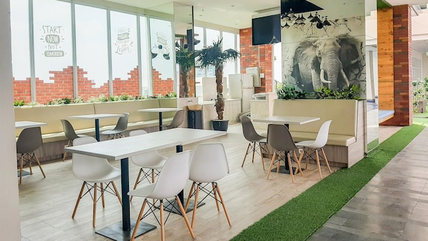 A modern restaurant with white tables and chairs, large windows, and a mural of an elephant. - Fancy And Comfy Studio At B Residence Apartment (Pagedangan)