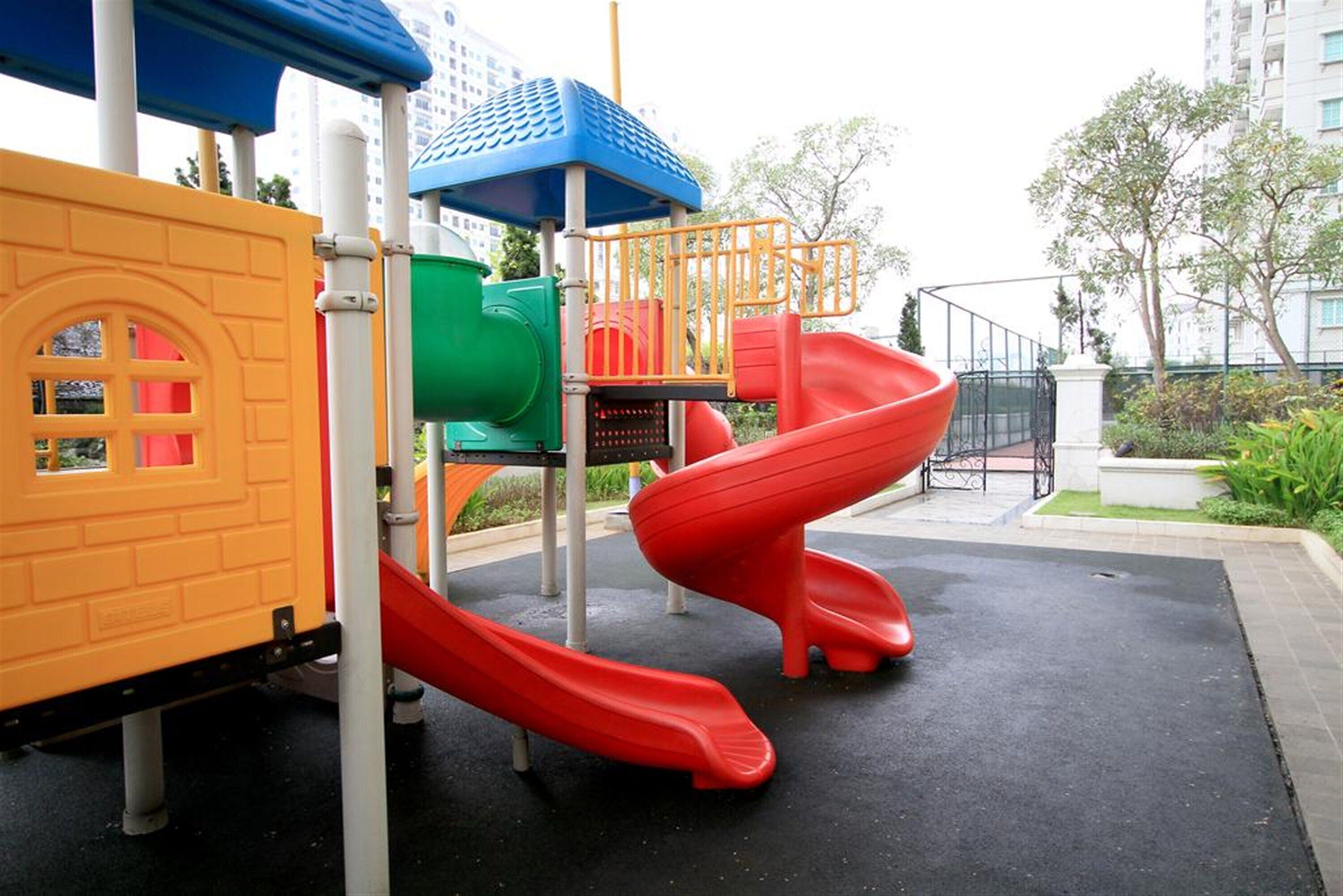 A playground with a red slide, a green climbing area, and a yellow playhouse.
