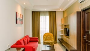 Una sala de estar moderna con un sofá rojo, un sillón estampado, un televisor montado en un panel de madera y un ventanal con cortinas.