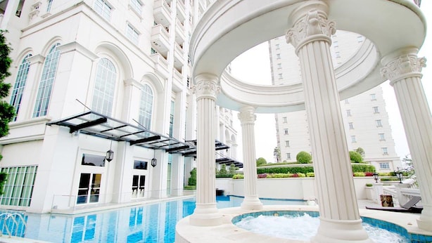 Un área de piscina interior lujosa con arquitectura clásica, que incluye columnas y una pérgola.