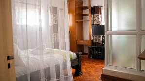 Une chambre à coucher avec un lit, une armoire en bois, une petite table et une fenêtre avec des rideaux.