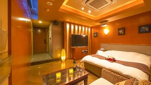 A hotel room with a bed, a TV, a bedside table with a bottle and glasses, and a mirror.