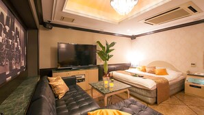 A hotel room with a sofa, a bed, a television, a nightstand, and a plant.