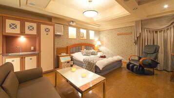 A hotel room with a bed, a sofa, a table, a chair, a desk, and a kitchenette.