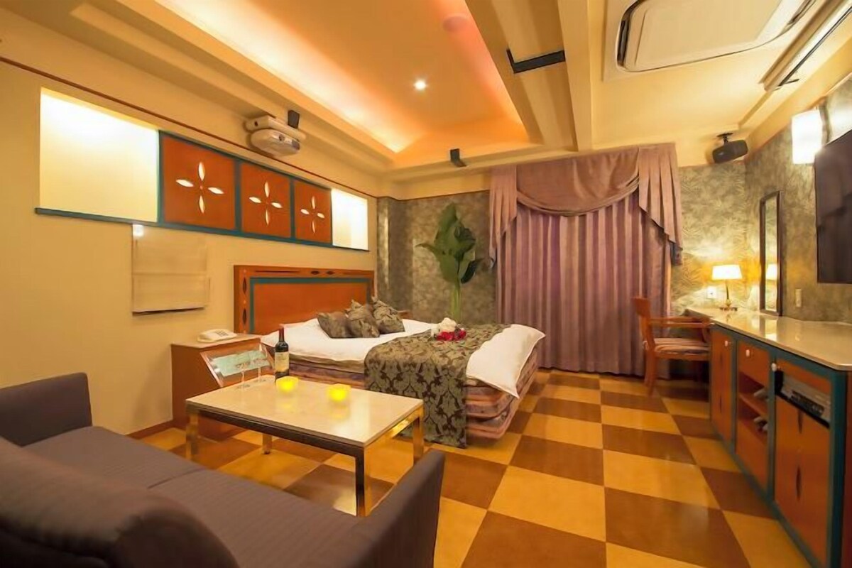 A hotel room with a bed, a desk, a chair, a table, and a check-in counter.