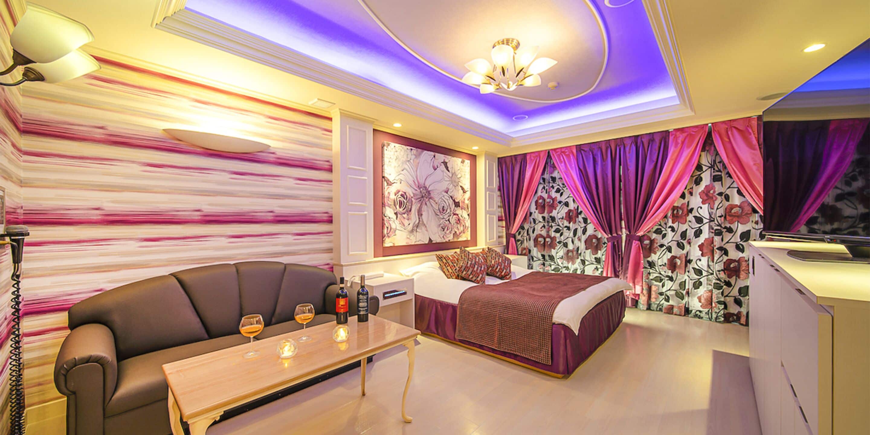 Ein modernes Schlafzimmer mit einer Couch, einem Bett, einem Nachttisch mit Weingläsern und einer Chandelüster.