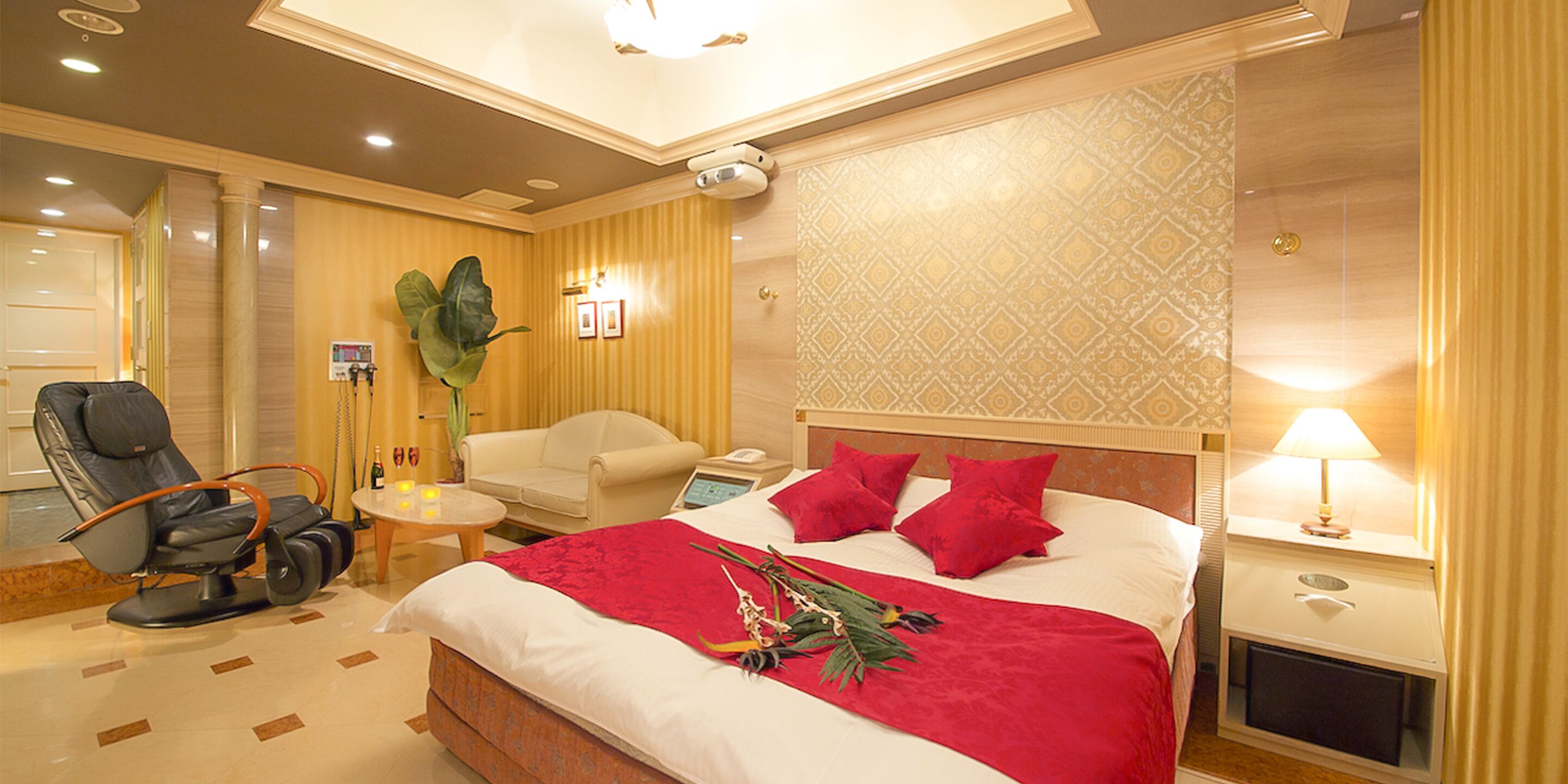 A hotel room with a bed, a massage chair, a small table with a lamp, and a nightstand.