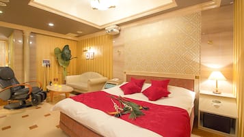 A hotel room with a bed, a massage chair, a small table with a lamp, and a nightstand.