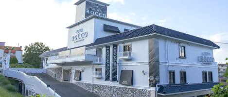 Un hotel de dos pisos llamado Hotel Rocco, con un diseño moderno, que cuenta con balcones y fachada de piedra.