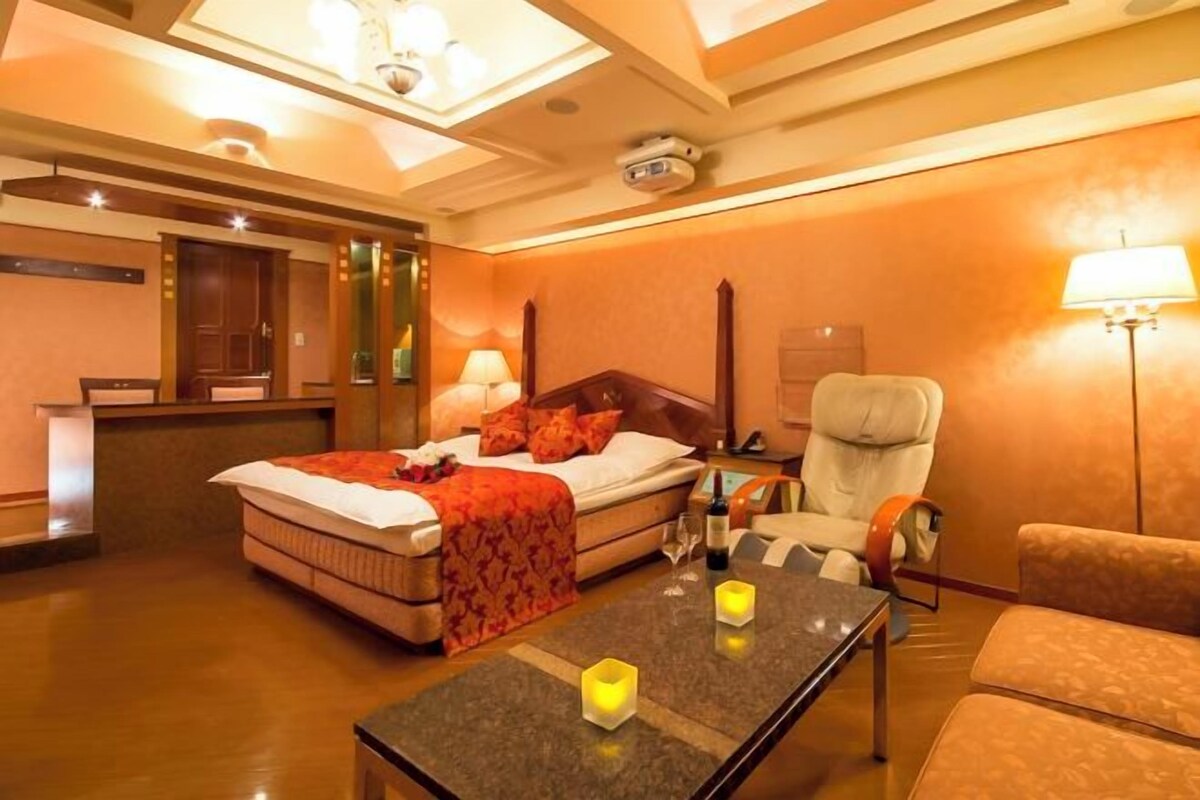 A hotel room with a bed, a desk, a chair, and a table with candles.