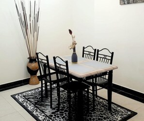 A dining area with a table and four chairs, a vase with a plant, and a patterned rug.