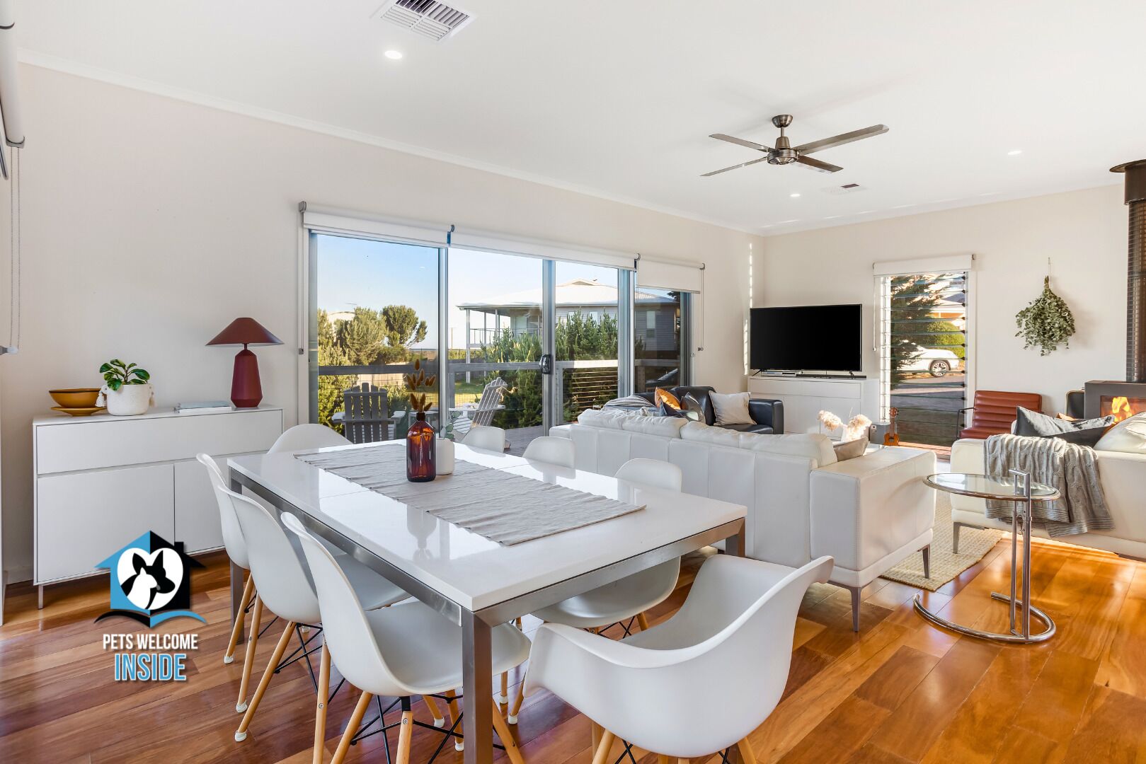 A modern living room with a white sofa, a dining table with chairs, a TV, and a fireplace.