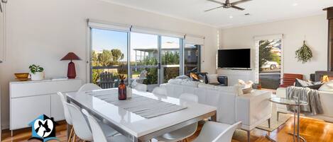 A modern living room with a white sofa, a dining table with chairs, a TV, and a fireplace.