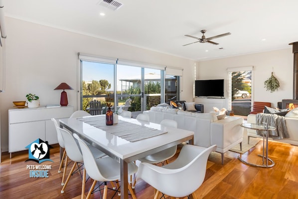 A modern living room with a white sofa, a dining table with chairs, a TV, and a fireplace.