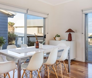 A modern dining area with a glass-top table, white chairs, and a view of the outside.