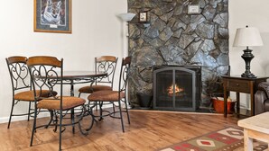 Uma sala de jantar com lareira de pedra, um quadro com imagem de animal e uma luminária.