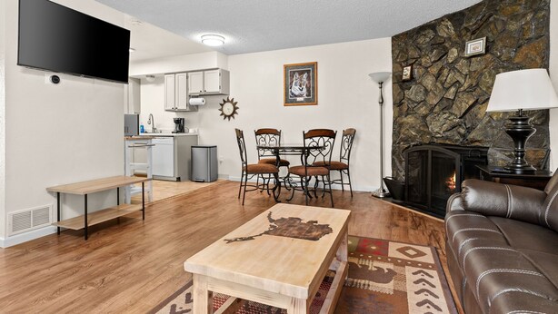 Uma sala de estar moderna com uma mesa de centro de madeira, um sofá de couro, uma lareira de pedra e uma área de jantar com mesa e cadeiras.