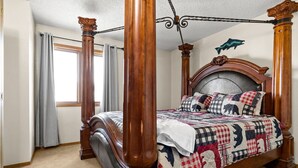 Uma cama com dossel, com colcha, cabeceira de madeira e cortinas.