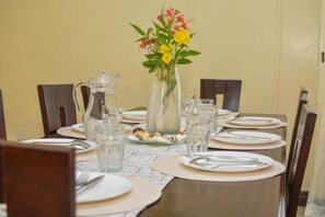 A dining table set with plates, cutlery, glasses, and a pitcher, with a vase of flowers in the center.
