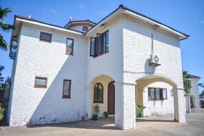 A two-story house with a white stucco exterior, a tiled roof, and a central entrance with an archway.