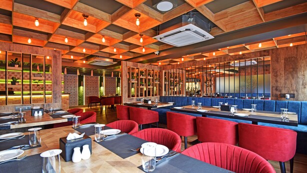 A restaurant with wooden ceiling panels, red upholstered chairs, and tables set for dining. - Treebo Sky Point (Jalpaiguri)