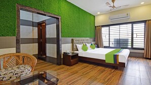 A hotel room with a bed, a chair, a nightstand, a mirror, and a window with curtains. - Treebo Sky Point (Jalpaiguri)