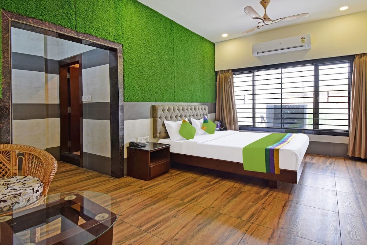 A hotel room with a bed, a nightstand, a chair, a glass table, and a green wall.