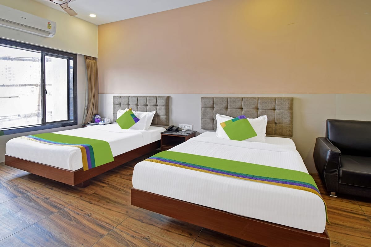 A hotel room with two beds, a window, an air conditioning unit, and a black leather chair.