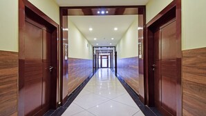A hallway with wooden doors, numbered 203 and 206, leading to a bright, tiled area with ceiling lights. - Treebo Sky Point (Jalpaiguri)