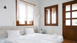 Une chambre d’hôtel avec deux lits, une tête de lit en bois, une table de chevet, une fenêtre avec un cadre en bois et une porte avec un panneau de verre.