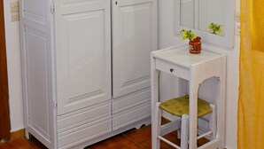 Une pièce avec une armoire blanche, une petite table avec un miroir et un téléviseur fixé au-dessus de l’armoire.