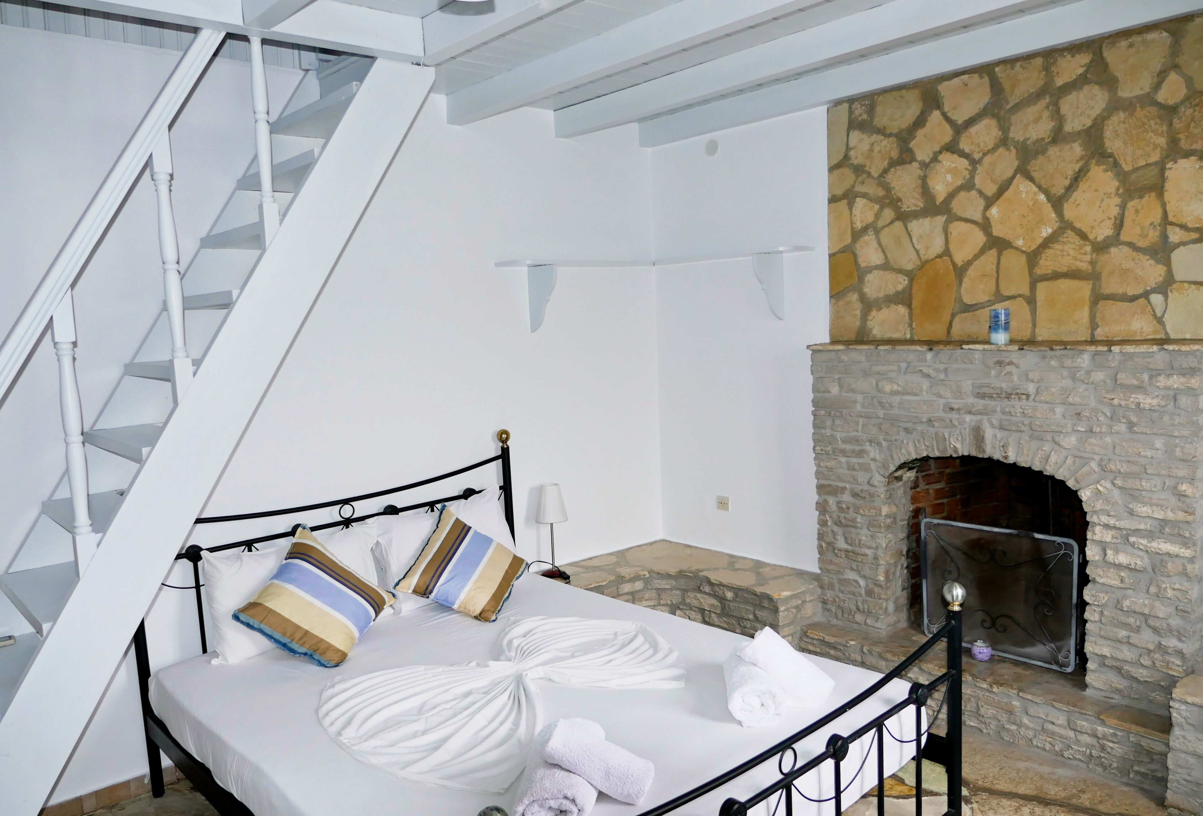 A bedroom with a bed, pillows, a fireplace, and a staircase.