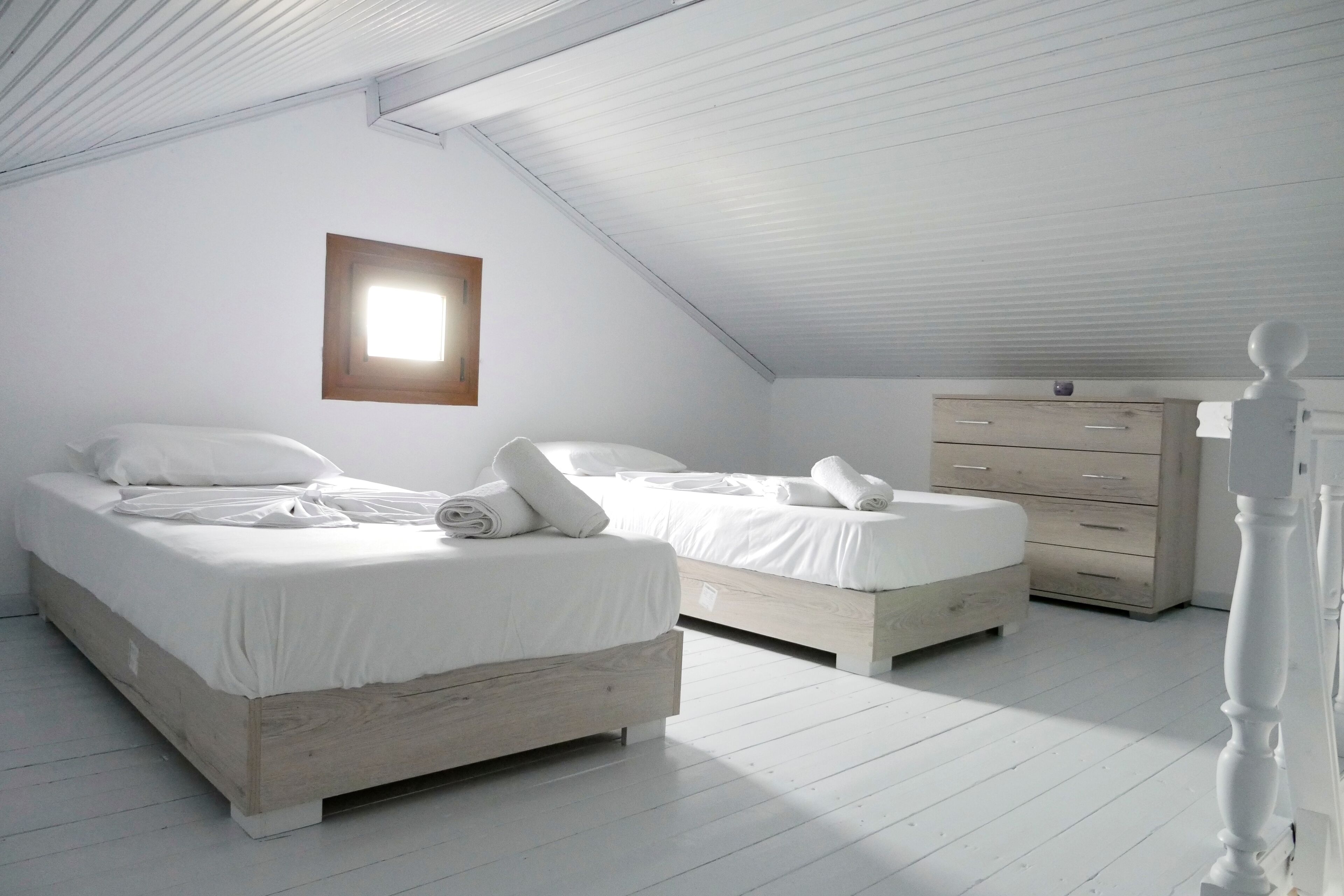 A bedroom with two beds, a dresser, and a window.
