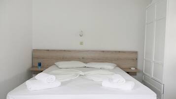 Una cama bien tendida con toallas dispuestas en un lazo, una mesita de noche con un vaso de agua y un armario a la derecha.